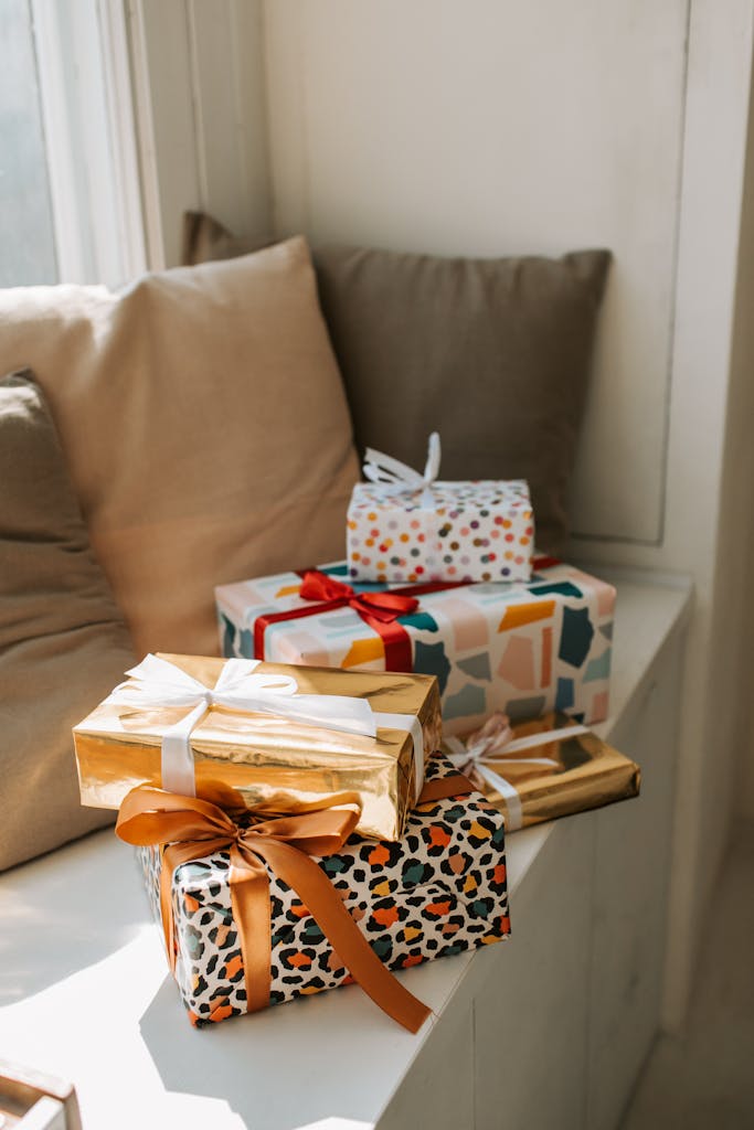 A variety of gift boxes wrapped with colorful paper and ribbons on a cozy window seat, creating a festive atmosphere.