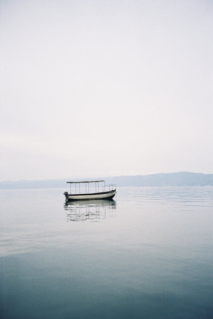 Peaceful scene of a lone boat floating on a calm lake with a clear sky.